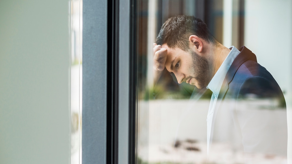 Ein Mann im Business-Outfit lehnt erschöpft an einem Fenster