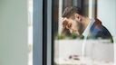 Ein Mann im Business-Outfit lehnt erschöpft an einem Fenster