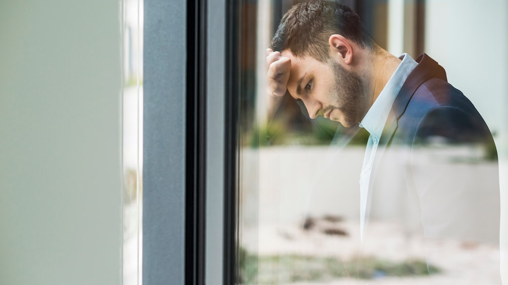 Ein Mann im Business-Outfit lehnt erschöpft an einem Fenster