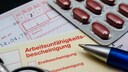 Krankmeldung verspätet Krankenkasse: Auf einer Arbeitsunfähigkeitsbescheinigung liegen ein Stift, Tabletten und ein Rezept