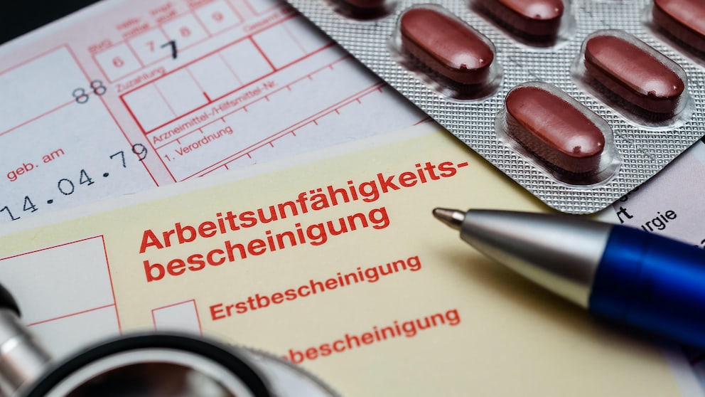 Krankmeldung verspätet Krankenkasse: Auf einer Arbeitsunfähigkeitsbescheinigung liegen ein Stift, Tabletten und ein Rezept