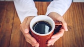 Kaffee Leber: Ein Mann hält eine Tasse Kaffe in seinen Händen