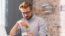 Ein Mann schaut aufs Smartphone während er in einen Apfel beißt