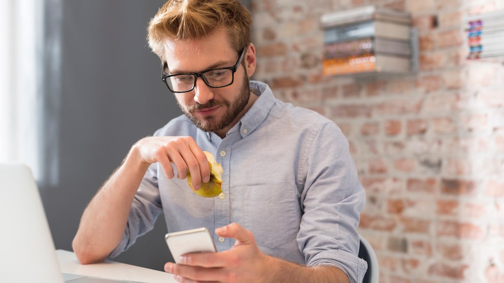 Ein Mann schaut aufs Smartphone während er in einen Apfel beißt