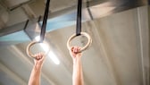 Ring Muscle-ups: Ein Mann fässt zwei Trainingsringe an