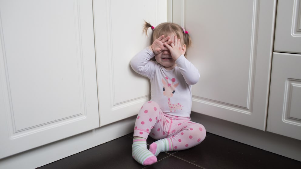 Ein kleines Mädchen sitzt auf dem Boden, hält die Hände an den Kopf und weint