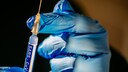Behandschuhte Hände halten eine Spritze mit Corona-Impfung