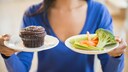 Eine Frau h&auml;lt zwei Teller, einmal mit Schokomuffin und einmal mit Gem&uuml;se hoch