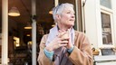 Frau mittleren Alters sitzt vor einem Café mit einer Tasse in der Hand