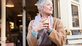 Frau mittleren Alters sitzt vor einem Café mit einer Tasse in der Hand