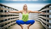 Blonde Frau auf einem Steg vor einem See in sportlicher Bekleidung in der Hocke