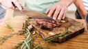Mann schneidet ein Steak auf einem Holzbrett
