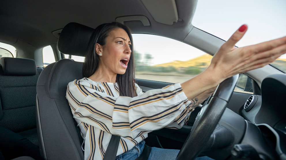 Frau gestikuliert wütend am Autosteuer