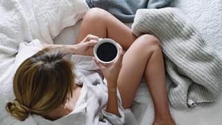 Wie wirkt Koffein auf den Schlaf? Eine junge Frau macht es sich mit einer Tasse Kaffee gemütlich