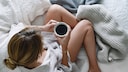 Wie wirkt Koffein auf den Schlaf? Eine junge Frau macht es sich mit einer Tasse Kaffee gemütlich