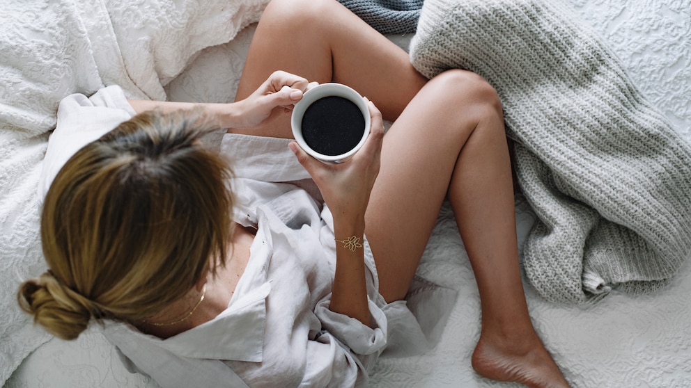Wie wirkt Koffein auf den Schlaf? Eine junge Frau macht es sich mit einer Tasse Kaffee gemütlich
