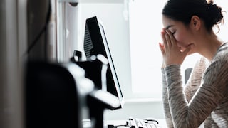 Junge Frau sitzt vor dem PC und fasst sich ins Gesicht