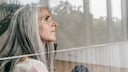Haarausfall während Menopause: Frau mit grauen Haaren am Fenster