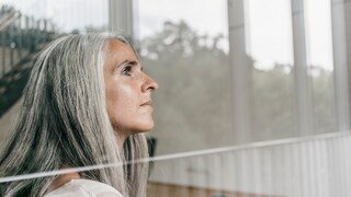 Haarausfall während Menopause: Frau mit grauen Haaren am Fenster