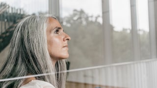 Haarausfall während Menopause: Frau mit grauen Haaren am Fenster