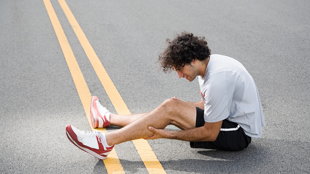 Ein Läufer sitzt auf der Straße und hält sich das schmerzende Bein