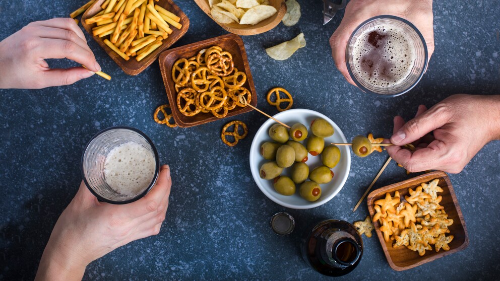 Tisch mit unterschiedlichen Snacks wie Chips, Brezeln und Oliven