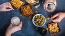 Tisch mit unterschiedlichen Snacks wie Chips, Brezeln und Oliven