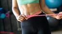 Ernährung abgestimmt aufs Fitnessziel: Frau mit misst sich ihren Taillenumfang