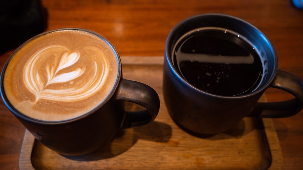 Ein Kaffee mit Milchschaum neben einem Americano