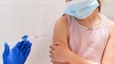 Ein Mädchen mit Mundschutz erhält eine Impfung in den Arm