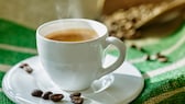 Kaffee entkoffeinieren: Eine weiße Kaffeetasse mit Kaffeebohnen im Hintergrund