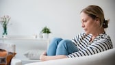 Depression Corona: Junge Frau hockt traurig im Sessel