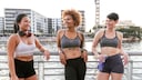 Drei jungen Frauen stehen fröhlich im Sport-BH an einem Geländer
