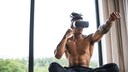 Muskulöser, junger Mann macht mit VR-Brille Box-Bewegungen im Schneidersitz