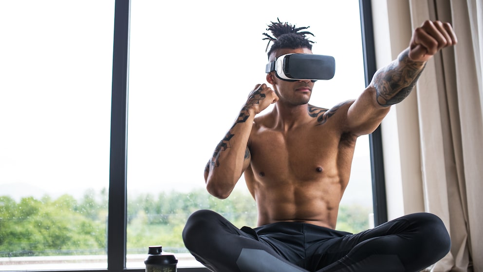 Muskulöser, junger Mann macht mit VR-Brille Box-Bewegungen im Schneidersitz