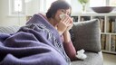 Erkältungssymptome: Eine Frau liegt mit Decke auf Sofa und putzt sich die Nase