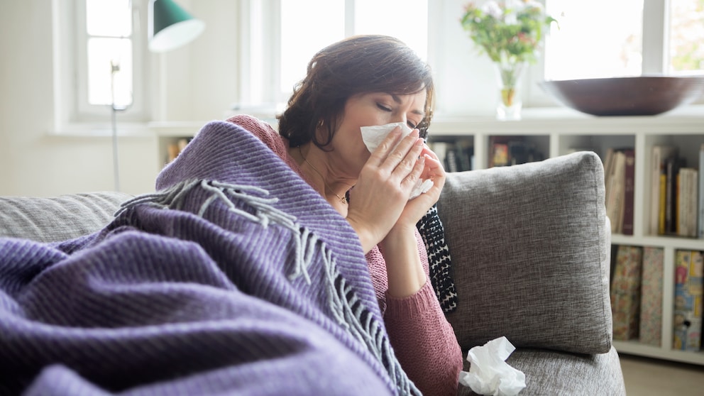 Erkältungssymptome: Eine Frau liegt mit Decke auf Sofa und putzt sich die Nase