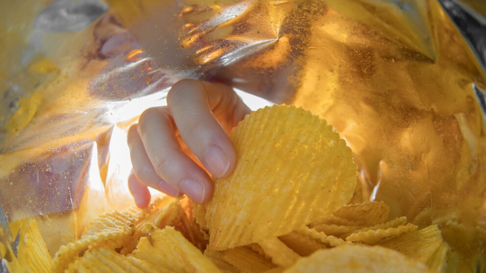 Eine Hand greift in die Chips-Tüte