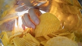 Eine Hand greift in die Chips-Tüte