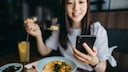 smartphone essen: Junge Frau isst und guckt auf ihr Handy