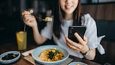 smartphone essen: Junge Frau isst und guckt auf ihr Handy