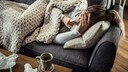 corona-symptome: Frau liegt krank auf ihrem Sofa