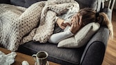 corona-symptome: Frau liegt krank auf ihrem Sofa