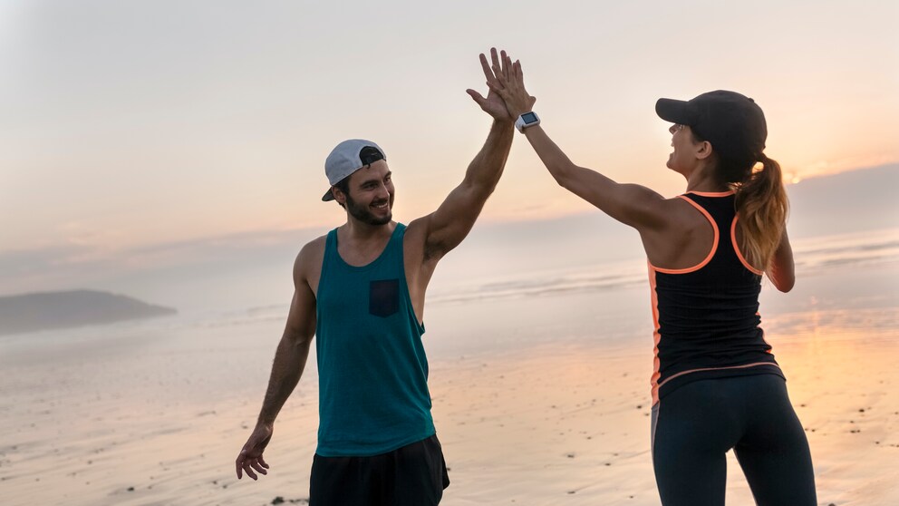 Junges sportliches Paar macht High Five am Strand