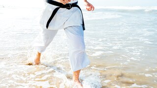 Mann im Karate-Gi läuft durch Meeresbrandung