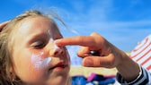 Mädchen wird mit Sonnecreme im Gesicht eingecremt