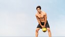 Junger, fitter Mann macht Kettlebell Swing am Strand
