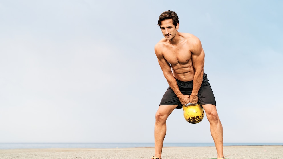 Junger, fitter Mann macht Kettlebell Swing am Strand