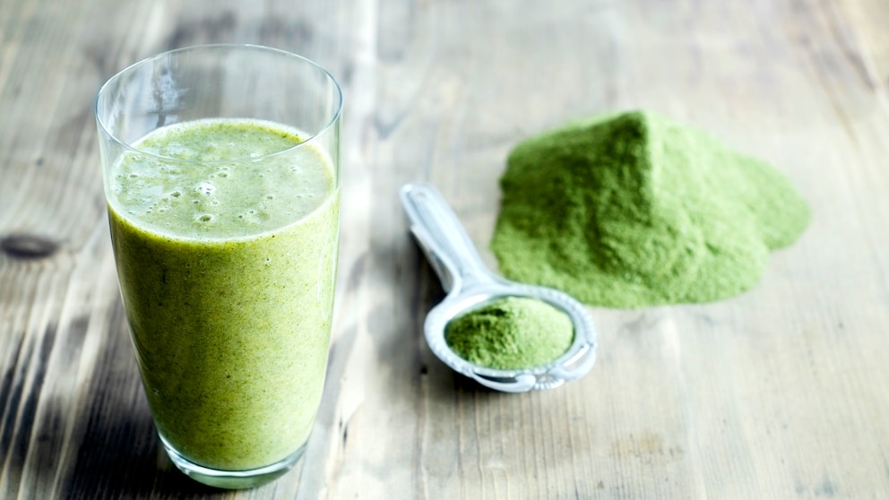 Eine Schale mit Moringa-Pulver und den Blättern des Moringa-Baums als Deko daneben