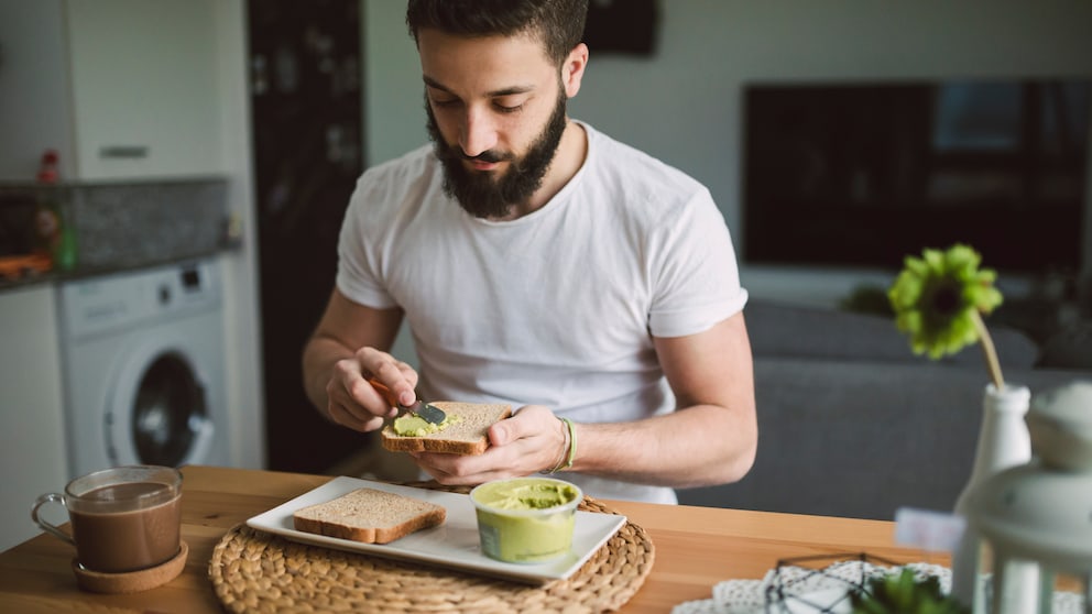 Mann schmiert sich Humus aufs Brot